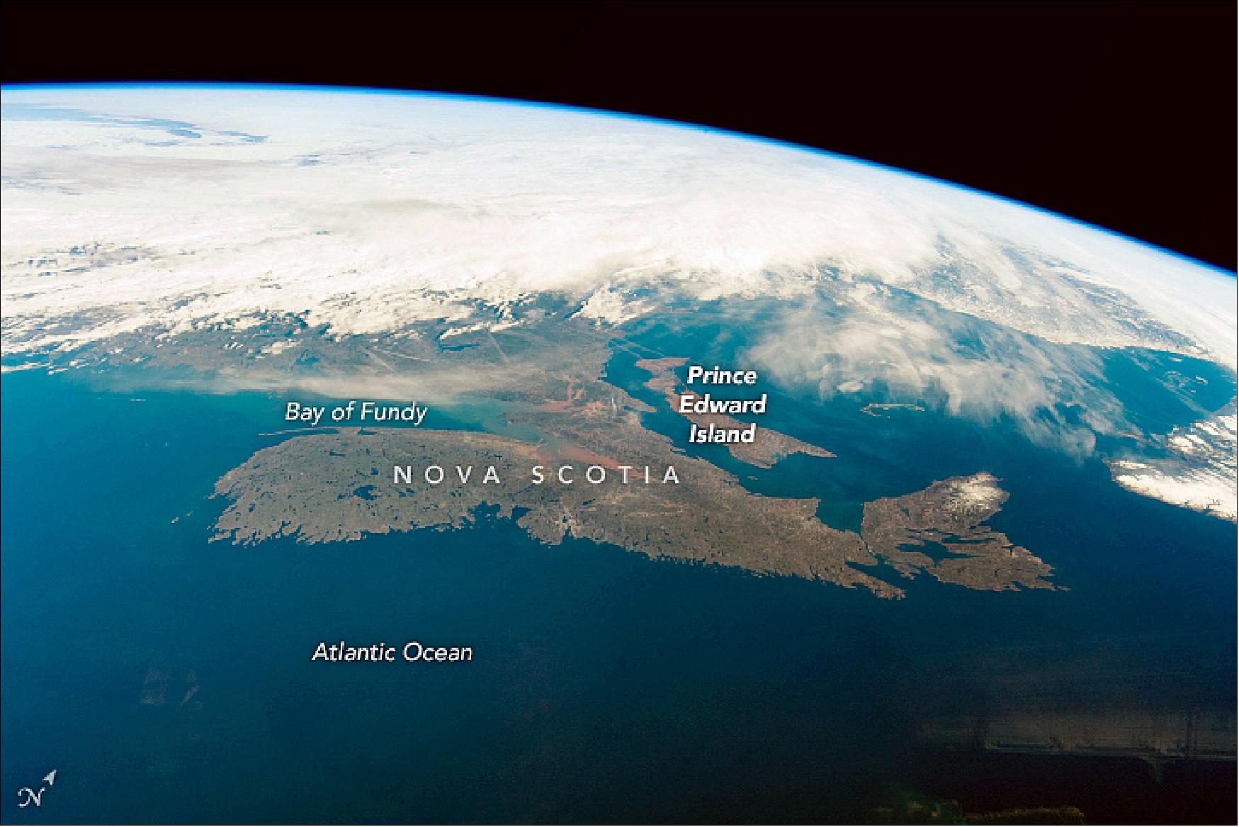 Figure 72: Taken 2 minutes and 18 seconds later, the second view is not only reversed—north to the right instead of the left and the Atlantic in the foreground—but the Sun is behind the camera and there is more color contrast. Land surfaces are brighter than the sea surface, which appears in a generally uniform color. The rounded southern end of Nova Scotia is prominent, having been almost lost to view in the first image. Coastline detail is much reduced. The warm tone of sediment at the head of the Bay of Fundy has become visible, and a hint of snow is visible at the northern end of the peninsula (image credit: Astronaut photographs ISS059-E-59135 and ISS059-E-52689 were acquired on 7 May 2019, with a Nikon D5 digital camera using 50 mm and 35 mm lenses (respectively) and are provided by the ISS Crew Earth Observations Facility and the Earth Science and Remote Sensing Unit, Johnson Space Center. The images were taken by a member of the Expedition 59 crew. Caption by M. Justin Wilkinson and Susan Runco)