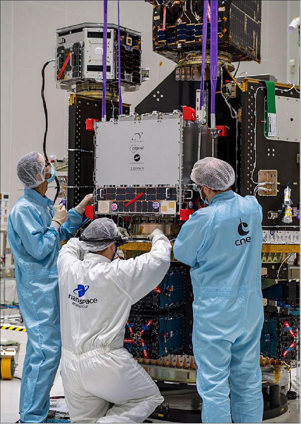Figure 12: Technicians performing payload integration of the D-Orbit ION CubeSat deployer carrying 12 Flock 4v SuperDoves, with Planet’s logo clearly visible. The remaining 14 SuperDove satellites are housed inside the blue and black ISL QuadPack deployers visible on the lower deck (image credit: Arianespace)
